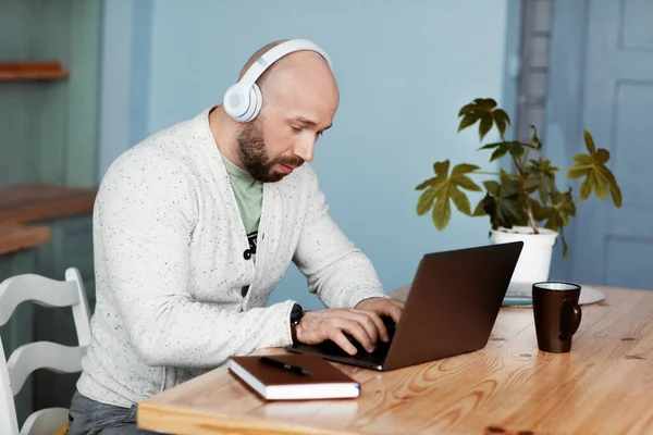 An attractive man with headphones is working at a computer at a computer in the kitchen. A businessman types text on a laptop and listens to music. Business without leaving home, work at home