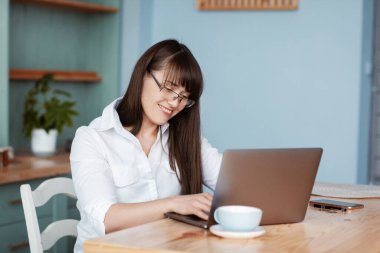 Mutfaktaki bilgisayarın başında çalışan güzel bir genç kız. Gözlüklü ve beyaz gömlekli bir kız postalarını kontrol edip kahve içiyor.