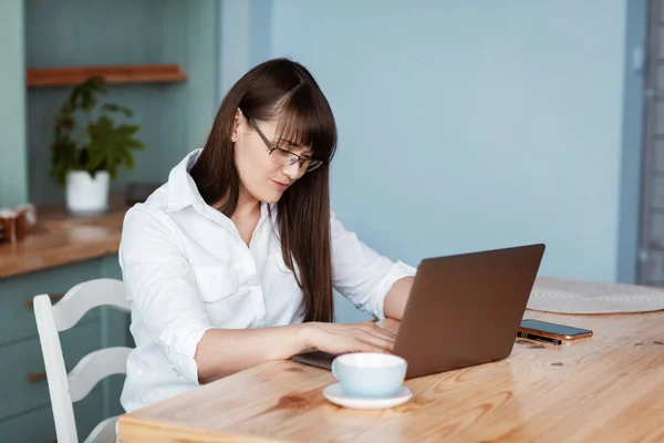 아름다운 부엌에 컴퓨터에서 일하고 있습니다 안경을 셔츠를 소녀가 편지를 확인하고 — 스톡 사진