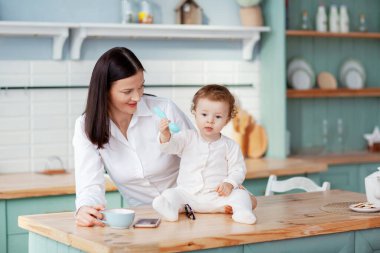 Güzel, genç bir anne, masadaki mutfakta çocukla iletişim kurup onu besler.