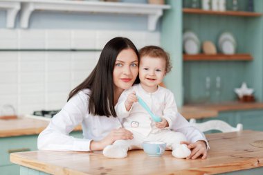 Güzel, genç bir anne, masadaki mutfakta çocukla iletişim kurup onu besler.