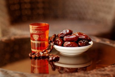Doğulu bir içecek, Arapça bir tespih ve cam bir masanın üzerindeki beyaz bir tabakta tarihler. İslam 'ın kutsal Ramazan ayı