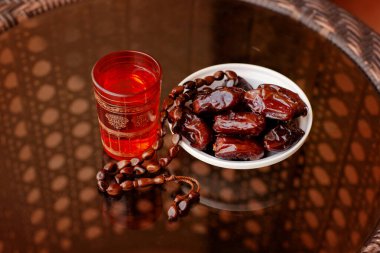 Doğulu bir içecek, Arapça bir tespih ve cam bir masanın üzerindeki beyaz bir tabakta tarihler. İslam 'ın kutsal Ramazan ayı