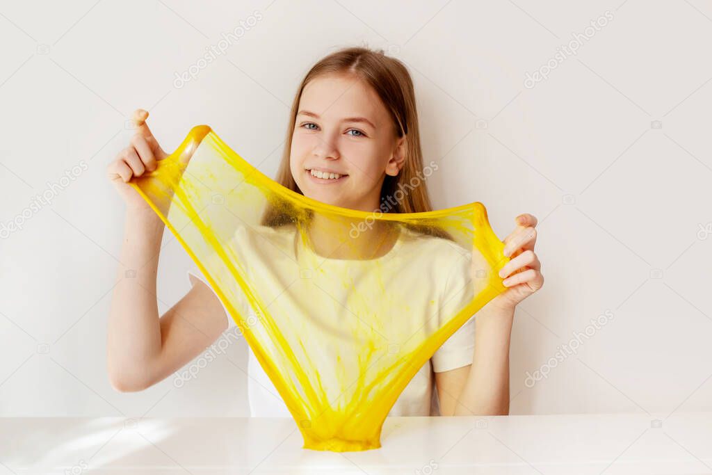 A charming girl smiles and plays with yellow slime. The girl holds in her hands and stretches the slime to transparency. Slime toy, anti-stress toy