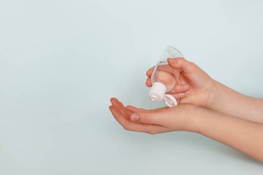 Kızların elleri mavi arka planda antibakteriyel jel kullanır. Sağlık koruma kavramı ve koronavirüsün önlenmesi. Yan görünüm, metin için boşluk