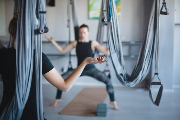 Back view of a girl practicing yoga asana with a hammock in the gym. Girl in the pose of a rider. Fitness aero yoga