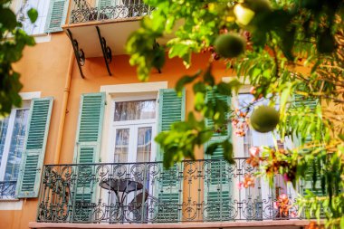 Dekoratif demir parmaklıklı balkon, masa ve açık kepenkler.
