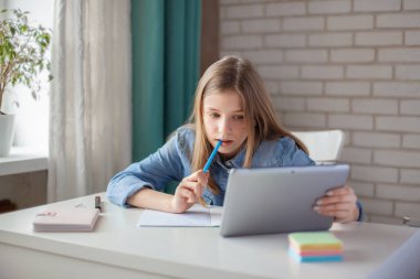 Şirin bir kız ödevini kendini tecrit sırasında tablet kullanarak yapıyor. Okul karantinaya alınırken. Sosyal mesafe, çevrimiçi öğrenme, uzaklık öğrenme