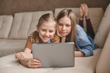 İki güzel kız evde bir tabletle oynuyorlar. Kız kardeşler karantina sırasında eğitim videoları izliyorlar. Karantina sırasındaki kişisel izolasyon, iletişim, sosyal uzaklık