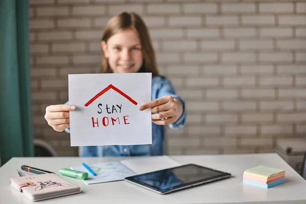 A beautiful teenage girl holds a sign saying stay at home. The girl recommends staying at home during the quarantine. Self-isolation, social distance