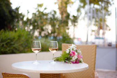 Bardakta beyaz şarap ve terasta masanın üzerinde bir buket narin çiçek var. Bir kafede romantik bir randevu.