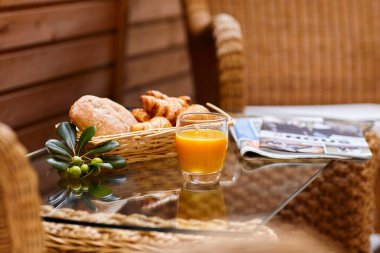 Taze hamur işleri, portakal suyu, zeytin dalı ve avludaki hasır masada duran taze bir gazete.