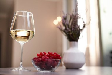 Vazoda bir buket, bir bardak beyaz şarap ve taze ahududu ve kırmızı üzümlü bir tabak var.