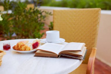 Taze hamur işleri, kahve, reçel ve açık bir kitap masanın üzerinde. Terasta ilginç bir kitapla kahvaltı.