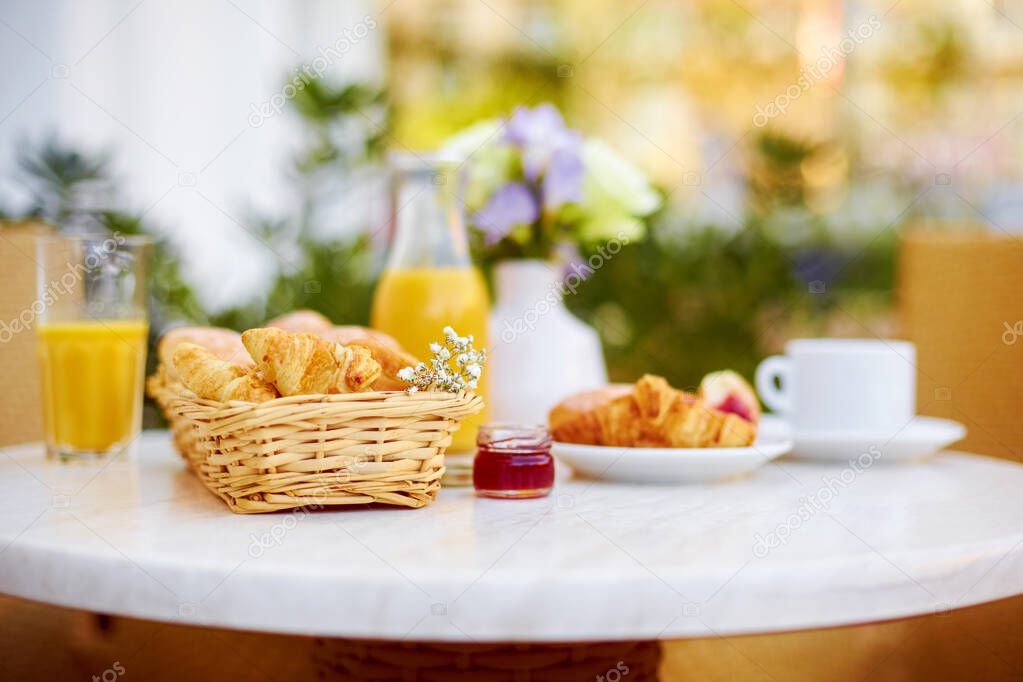 Fresh pastries, coffee, jam, a decanter and a glass of orange juice stand on a table decorated with a bouquet of delicate flowers on the terrace. Romantic Breakfast in the fresh air