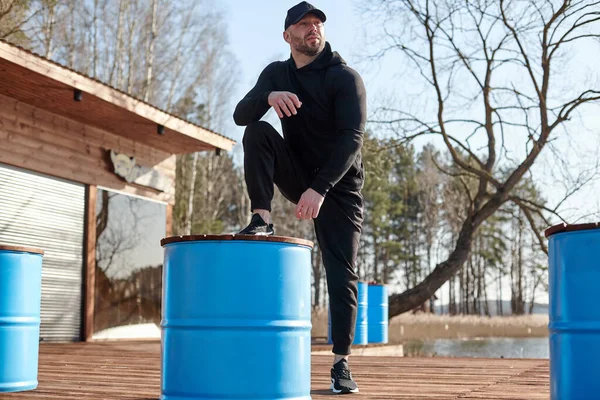 A tired athletic man takes a break during training. The man stretches out with his foot on the barrel and looks into the distance. The concept of fitness,sport, exercise, and lifestyle