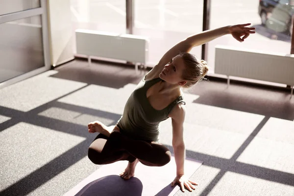 A beautiful girl is doing yoga against the background of panoramic Windows in the Studio. The girl performs balancing on one leg