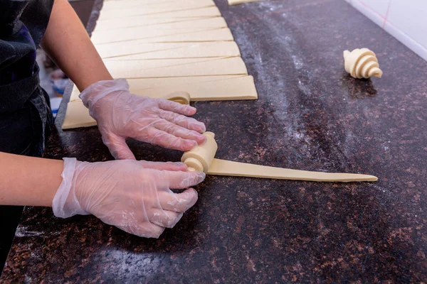 Un chef de pastelería en la cocina está haciendo pasteles. El chef enrolla la masa cortada en un croissant. Clase magistral en la cocina. El proceso de cocción. Paso a paso. Tutorial. Primer plano —  Fotos de Stock