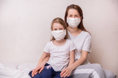 Koronavirüs karantinası kavramı. Tıbbi maskeli anne ve kız kendilerini virüslerden ve enfeksiyonlardan koruyorlar. Sağlık ve Tıp Teması.