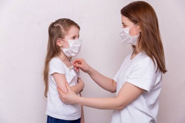 Koronavirüs karantinası kavramı. Genç bir kadın ve tıbbi maskeli kızı evde tecritte. Anne kızının sıcaklığını ölçer. Sağlık ve Tıp Teması.