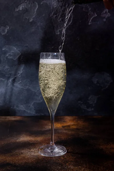 Barman pours champagne into a glass. Bubbles of champagne in a glass on a dark background. European lounge bar menu.