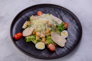 Koyu tabakta tavuk göğsü olan Sezar salatası. Ev yapımı tavuk fileto, kirazlı domates, parmesan peyniri, bıldırcın yumurtası, kraker ve sos. Avrupa mutfağı. Bir restoran veya kafe menüsünden yemek