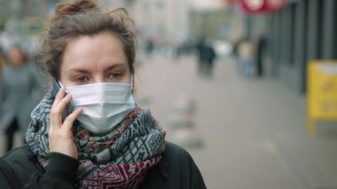 Yoğun sokakta telefonda konuşan genç bir kadın koruyucu maske takıyor.