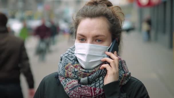 Женщина разговаривает по телефону на оживленной улице в защитной маске — стоковое видео