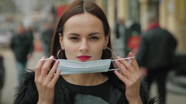 Egy fiatal nő védőmaszkot visel az utcán. — Stock videók