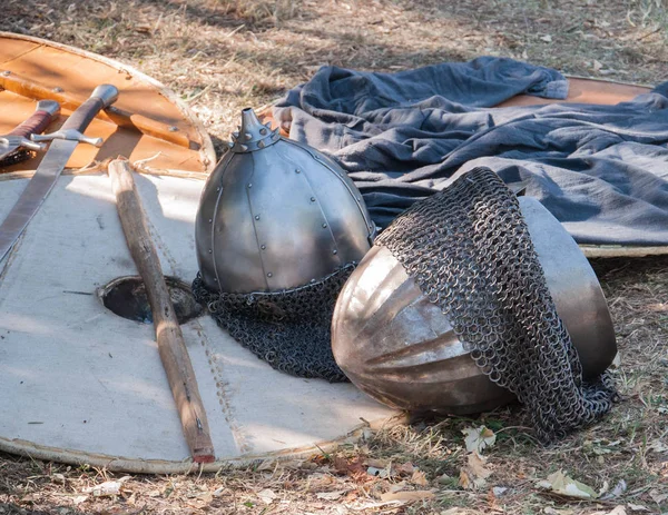 Outfit of a medieval warrior lying picturesquely at a medieval fair. Helmets, shields, chain mail, swords and axes.