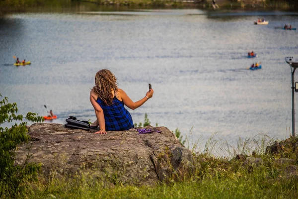 女孩在岩石上自拍 俯瞰公园里的湖面 — 图库照片