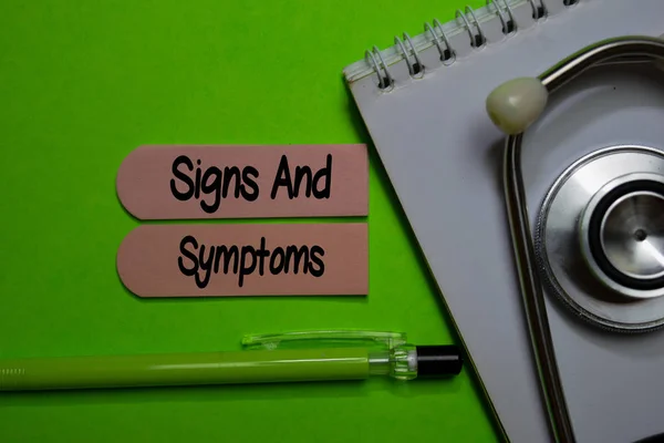 Signos y síntomas escriben en una nota adhesiva aislada en el escritorio de la oficina. Salud o concepto médico — Foto de Stock