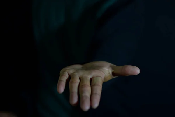 Young man showing hands it means of helping hand on dark black background. selective focus on finger