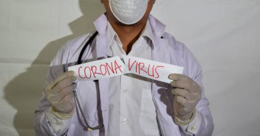 Bir doktor sağlık maskesi takıyor ve beyaz arka planda izole edilmiş bir korona virüsü kullanıyor..