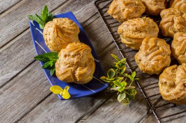 Elleri kremalı lezzetli kremalı büyük kremalı börekler eski ahşap arka planda nane yapraklı mavi oval çay tabağı boyası. Seçici odak.