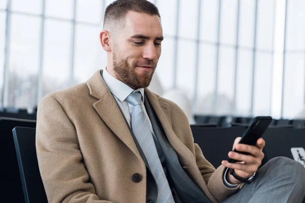 Lüks takım elbiseli kendine güvenen patron personelle görüşmeden önce e-postaları cep telefonuyla kontrol ediyor. Erkek profesyonel işveren havaalanı koridorunda otururken cep telefonundan mesaj yazıyor.