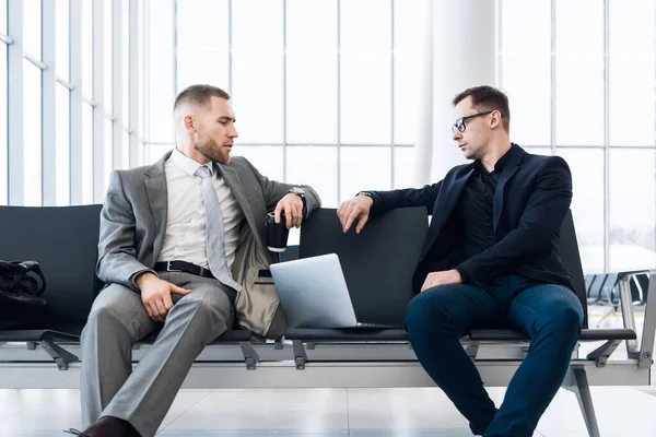 İş adamları havaalanı salonunda dizüstü bilgisayarda birlikte çalışıyorlar.