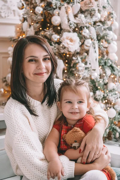 Feliz Natal e Boas Festas. Mãe alegre e sua linda filha menina se divertindo perto da árvore de Natal dentro de casa, sorrindo para a câmera . — Fotografia de Stock