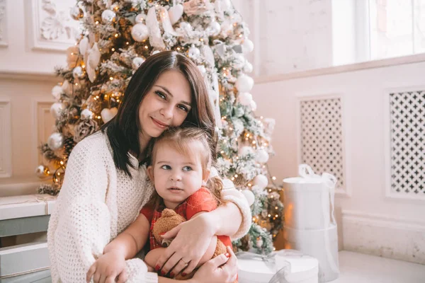 Feliz Navidad y Felices Fiestas. Alegre mamá y su linda hija se divierten cerca del árbol de Navidad en el interior, sonriendo a la cámara . — Foto de Stock