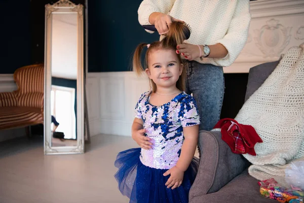 Мать расчесывает волосы своей маленькой дочери в красивом платье дома — стоковое фото