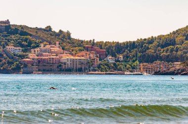 Grosseto, Toskana 'daki Tenda Gialla plajının önündeki Poggio Pertuso manzarasıyla denizde yüzen adam.