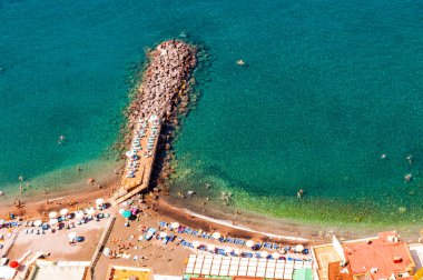 Napoli 'nin Meta ve Sorrento şehirleri yakınlarındaki Tyrhenian deniz koyunda turist, şezlong ve şemsiyelerle dolu sahildeki kayalık taşlı marinaları yukarıdan seyret.