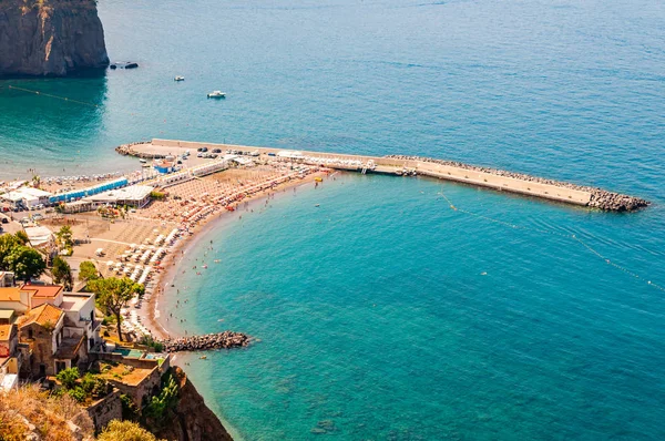 Vista desde arriba en los puertos deportivos de piedras rocosas en la playa llena de turistas, tumbonas, sombrillas en la bahía del mar Tirreno cerca de las ciudades de Meta y Sorrento en la región de Nápoles — Foto de Stock