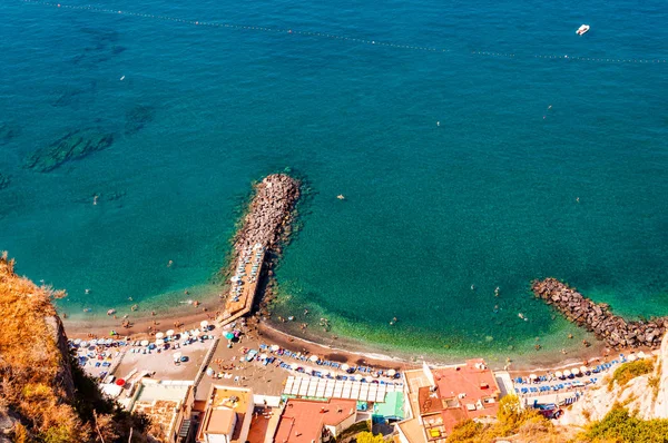 Vista de cima em pedras rochosas marinas na praia cheia de turistas, espreguiçadeiras, guarda-chuvas na baía do mar Tirreno perto de cidades Meta e Sorrento na região de Nápoles — Fotografia de Stock
