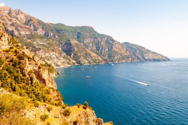 Positano 'nun güzel manzarası. Yüksek dağların yakınındaki kayık ve yatlarla dolu Rocky kıyı şeridi. Positano şehri tepeler ve derin mavi Tyrhenian deniz sularıyla çevrili.