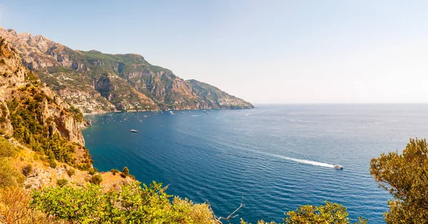 Positano 'nun güzel manzarası. Yüksek dağların yakınındaki kayık ve yatlarla dolu Rocky kıyı şeridi. Positano şehri tepeler ve derin mavi Tyrhenian deniz sularıyla çevrili.