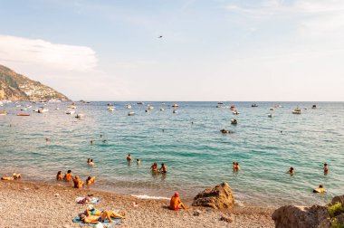 İnsanlar dinleniyor, güneşleniyor ve yüzüyor. Positano 'daki Tyrhenian Denizi' nin güzel çakıl taşları sahillerinde. İtalya 'nın Campania kentindeki kayalık dağlarda inanılmaz bir ortaçağ şehri.