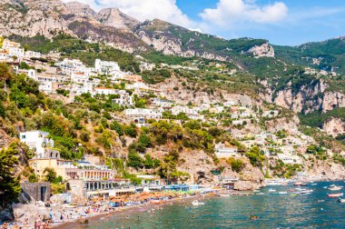 İnanılmaz Positano şehri kayalık arazide, plajdaki insanlar, tekneler deniz turlarına gelip gidiyor, apartmanlar ve iş yerleriyle dolu gezinti alanları.