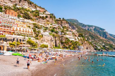 Ortaçağ Positano 'sunun kayalık manzarası, plajdaki insanlar, rahat caddelerde yürüyen turistler ve apartman ve iş yerleriyle dolu gezinti yerleri.