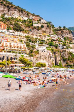 Ortaçağ Positano 'sunun kayalık manzarası, plajdaki insanlar, rahat caddelerde yürüyen turistler ve apartman ve iş yerleriyle dolu gezinti yerleri.